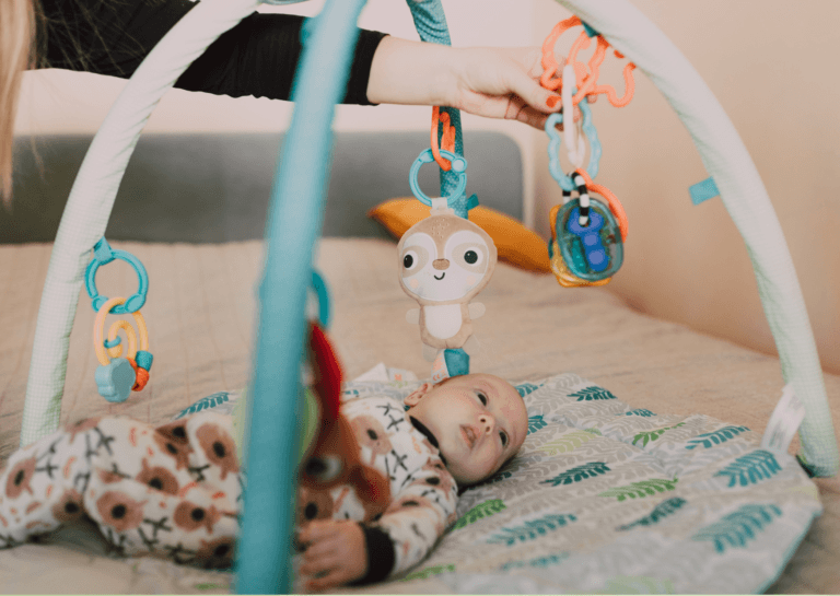 Baby lying on an activity gym, reaching for colorful hanging toys that stimulate play and development.