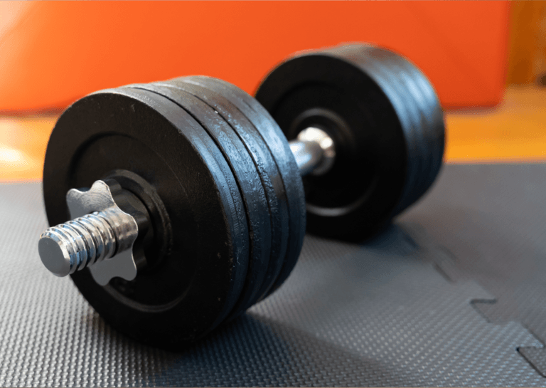 Adjustable silver dumbbell with four weights on each side, placed on a fitness mat for versatile strength training.