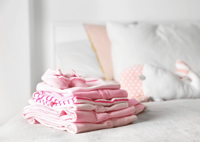 Neatly folded pink baby bedding set on a crib, featuring soft fabrics and adorable patterns, perfect for a nursery.