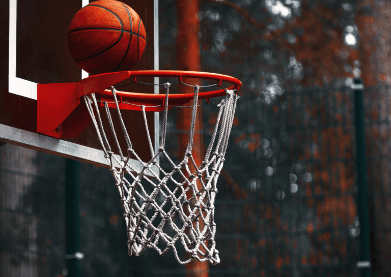 Basketball net with a basketball just about to go in, set against a blurred background evoking an autumn atmosphere.