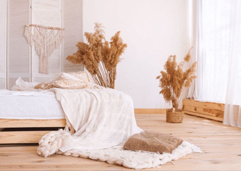 Bright, light-toned bedroom with white and light oak decor, featuring a decorative white throw on the bed, pampas grass accents, and a dreamcatcher, naturally lit during the day.