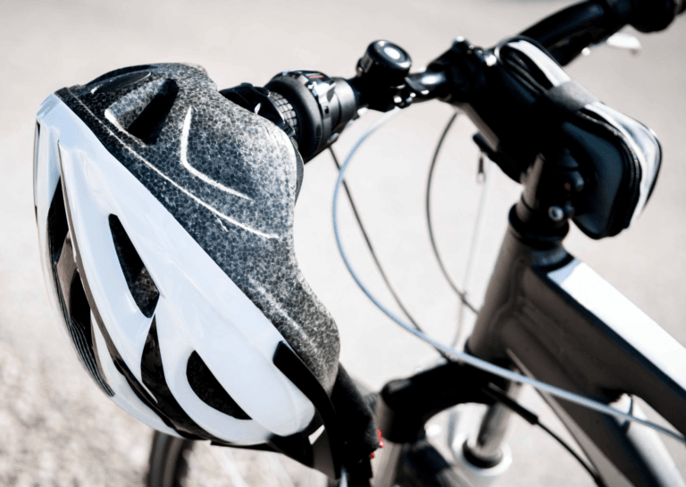 Close-up of the front of a mountain bike as if standing by the saddle, featuring a white mountain bike helmet hanging from the handlebars.