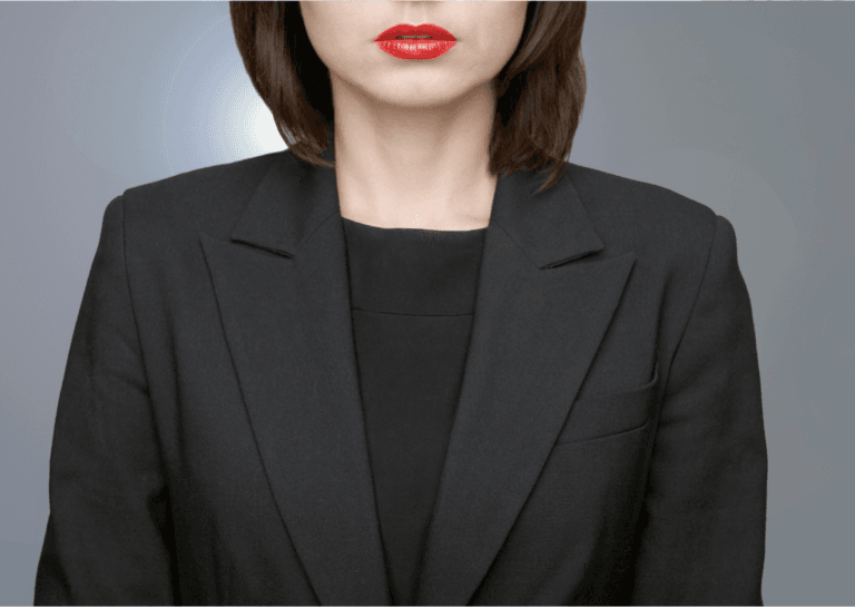 Woman wearing a dark blazer and red lipstick, shown from the waist up, focusing on her upper abdomen to just above her lips.