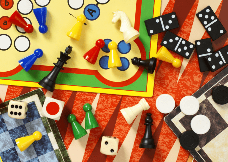 Various board games photographed from above, overlapping each other, showcasing different angles of game boards like 'Sorry,' along with game pieces and dice.