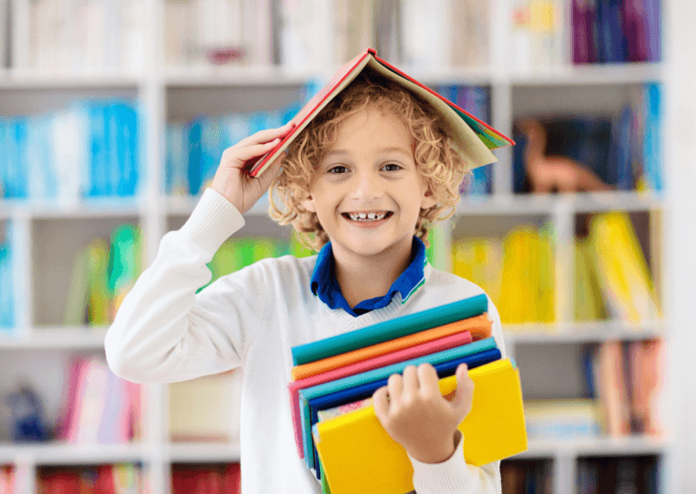 Young boy, around 10 years old with curly blonde hair, holding a notebook in one arm while balancing an open book on his head in a peaked shape with his other arm. In the background, a library-like scene filled with numerous books on shelves creates a cozy, intellectual atmosphere.