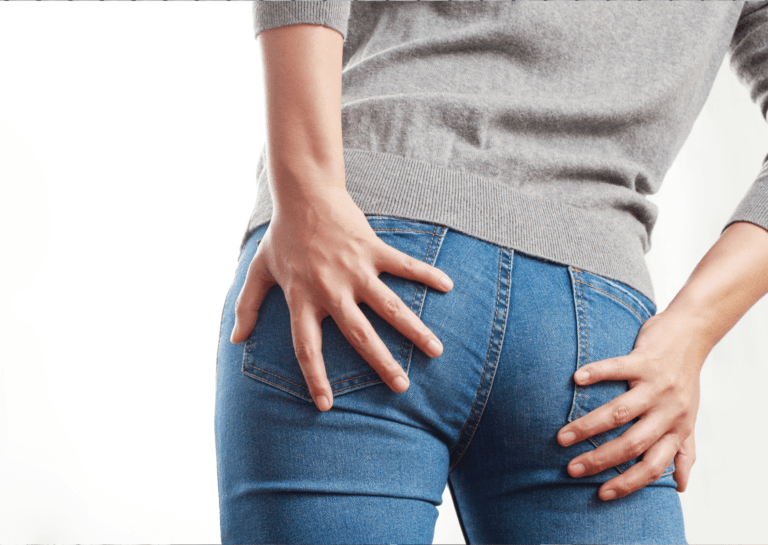 Woman in blue jeans and a gray sweater, with her hands on her hips, showing only her midsection in the frame.