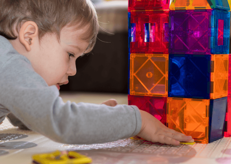 Toddler closely building with colorful magnetic construction toys, showcasing creativity and focus on a playful surface.