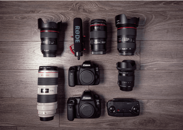 Two Canon cameras and several camera lenses lying on a brown wooden floor, captured from above, showing the front view of the cameras.