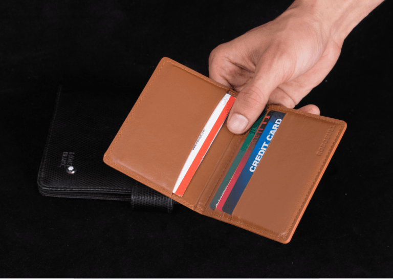 Man's hand holding a light brown cardholder, which is open to display the cards inside.