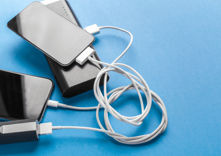 Two black smartphones being charged by black power banks with white cables on a blue background.