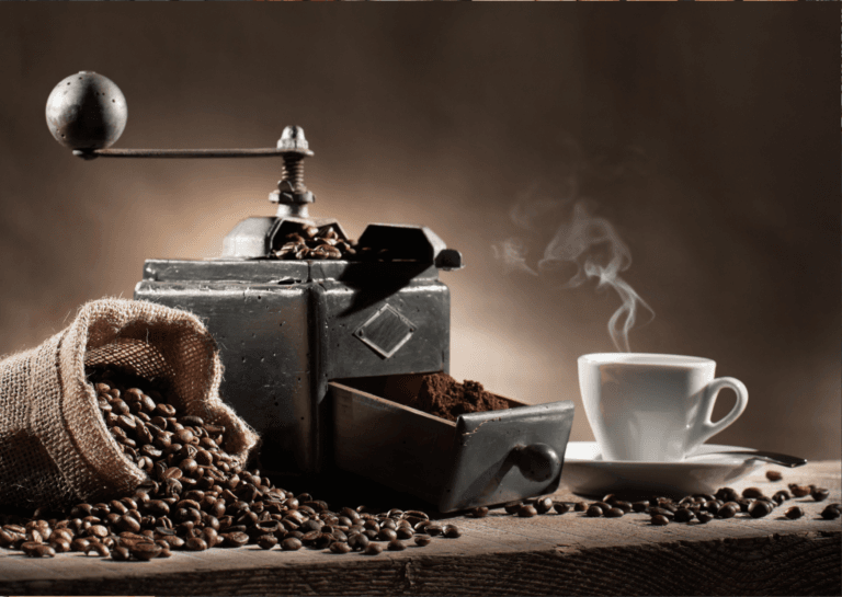 Vintage coffee grinder with a lying burlap sack filled with coffee beans spilling out, accompanied by a freshly brewed cup of steaming coffee, all presented in warm brown tones.