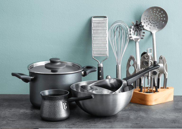 Cookware utensils including various pans, a grater, garlic press, and wooden spoons displayed on a dark gray countertop, with a light green background.