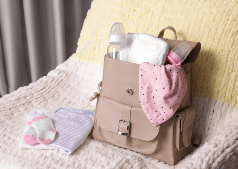 Brown diaper bag filled with diapers, a milk bottle, socks, and other essentials, ready for a day out with a baby.