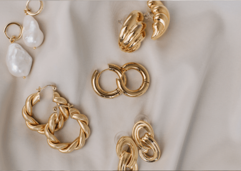 Five different gold earrings displayed on an elegant fabric, showcasing their unique designs and sparkling details.