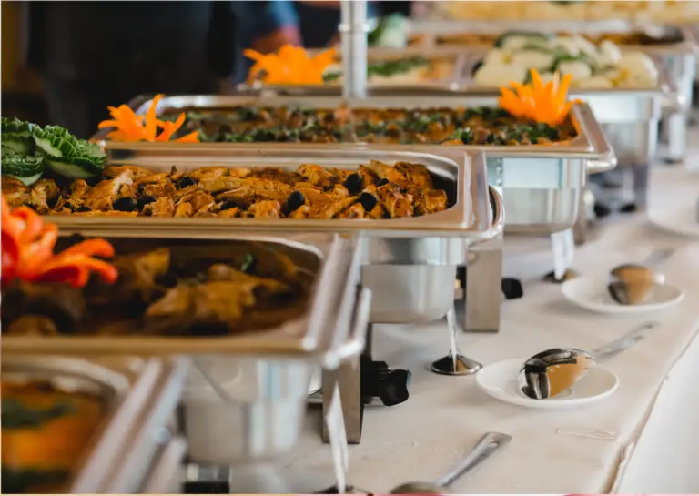 Four chafing dishes with warm food arranged on a table, prepared for an event.