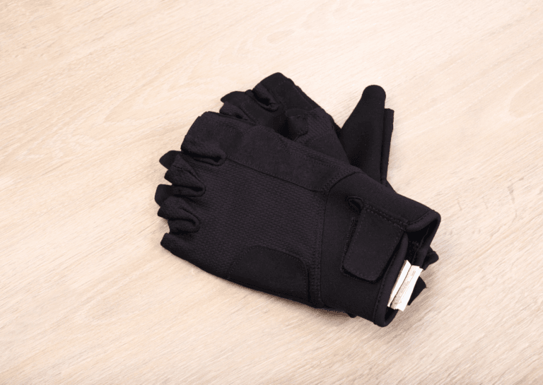 Fingerless fitness gloves stacked on top of each other with the inside facing up, resting on a light wooden floor.