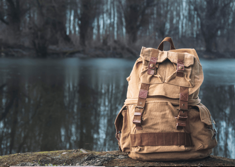 Brown backpack resting on a large rock in front of a serene lake, surrounded by a wooded area.