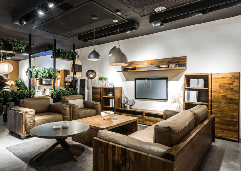 Showroom-styled living room with a rectangular brown coffee table beside a round table, wall-mounted TV, two large armchairs, and a three-seater sofa.