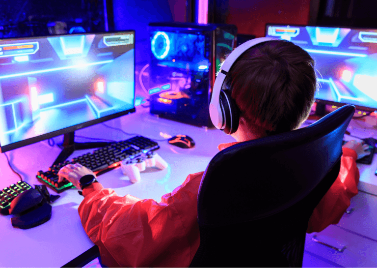 Boy gaming at his desk on a gaming PC, illuminated by bright gaming colors, captured from behind.