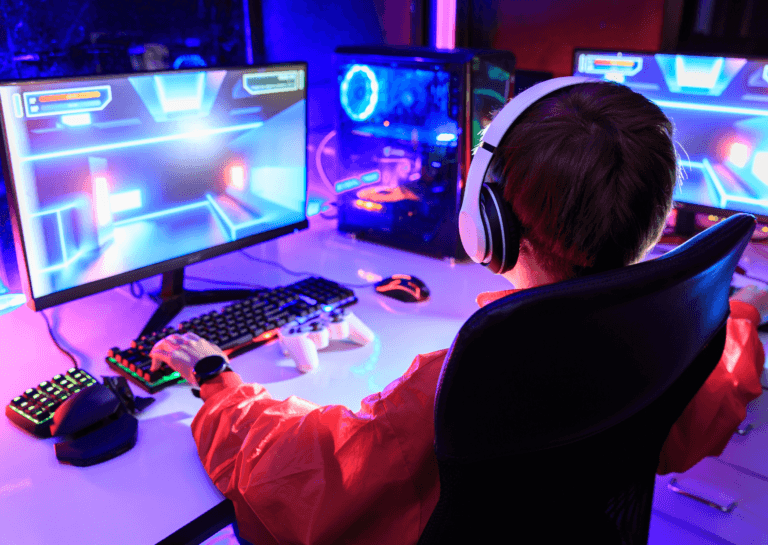 Boy gaming at his desk on a gaming PC, illuminated by bright gaming colors, captured from behind.