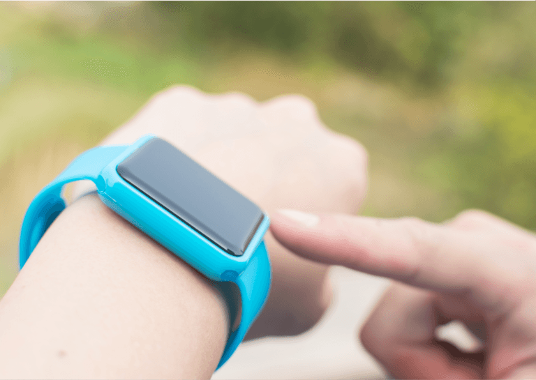 Close-up of blue health-monitoring wearable on a person's wrist, showing their hand interacting with the device.