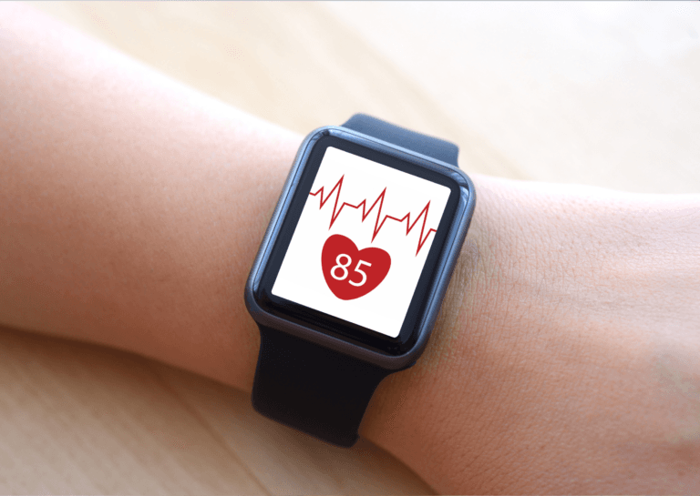 Close-up of a heart rate monitor watch on a wrist, featuring a white screen displaying a red heart rate with a red heart icon below showing the number 85.