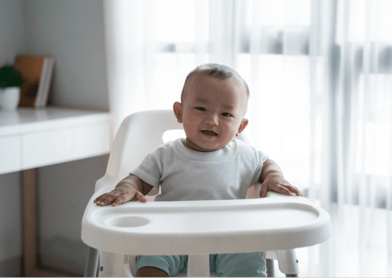 Laughing toddler in a white shirt sitting happily in a high chair.