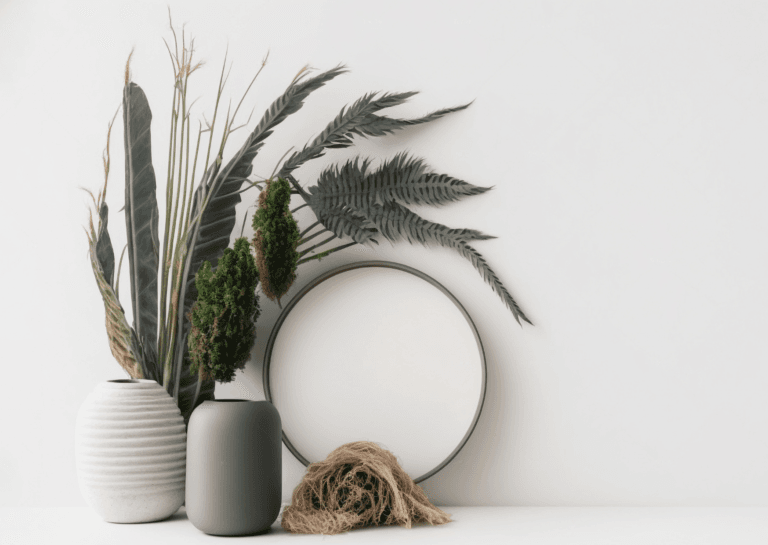 Home decor arrangement with three small vases holding faux flower stems, positioned next to a round mirror against a white wall.