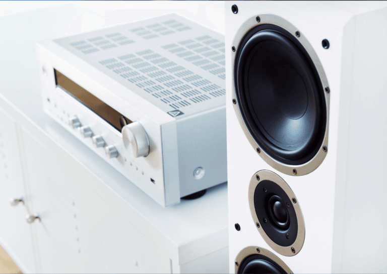 Home theater system featuring a white amplifier and a tall speaker with three black speakers inside, displayed on a white cabinet against a completely white background.