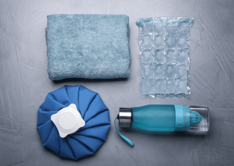 Ice pack therapy setup featuring a folded towel, an ice cube mat, a water bottle, and additional accessories for heat therapy.