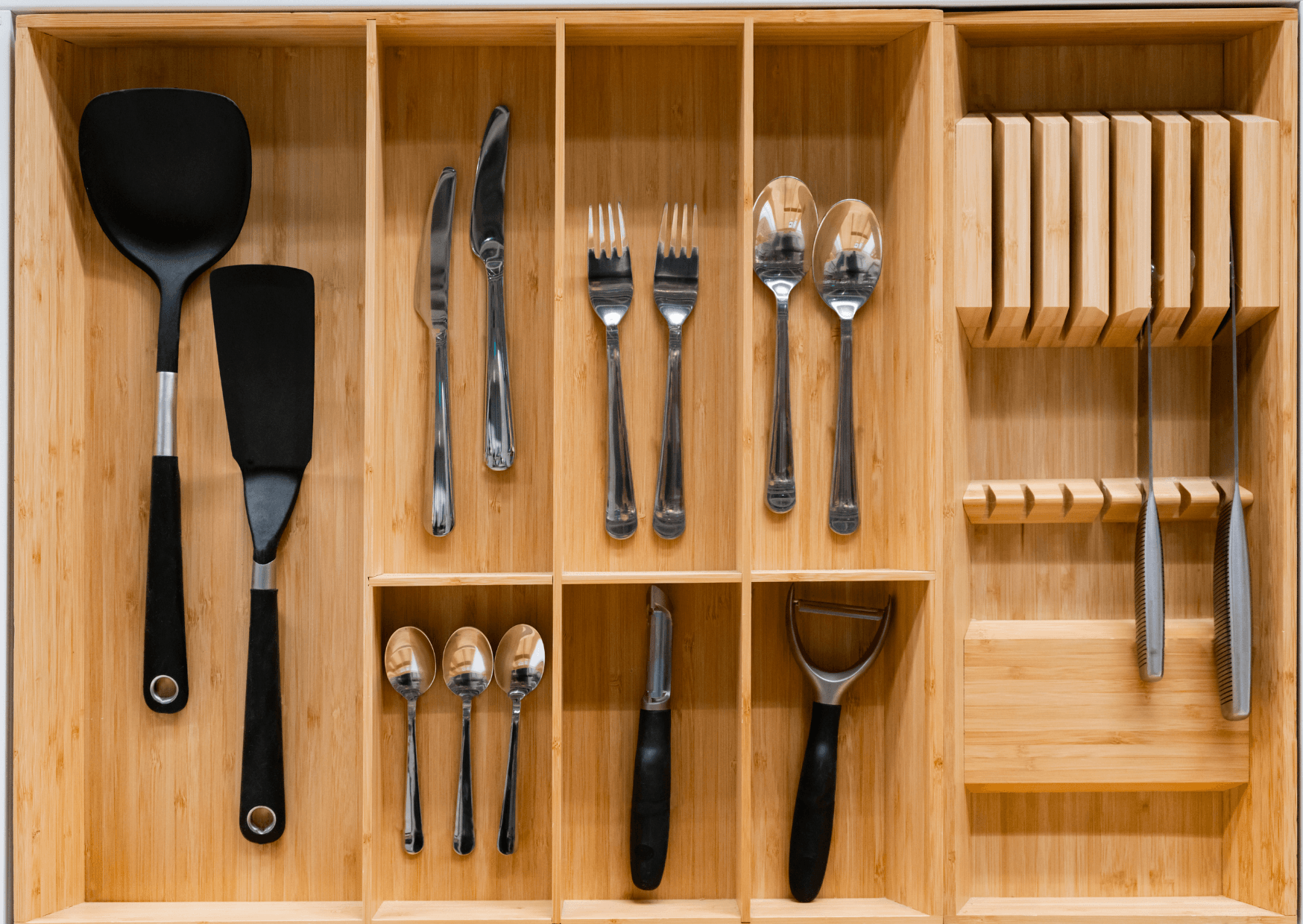 Organized wooden cutlery tray containing various utensils, including forks, knives, serving spoons, and spatulas arranged neatly.