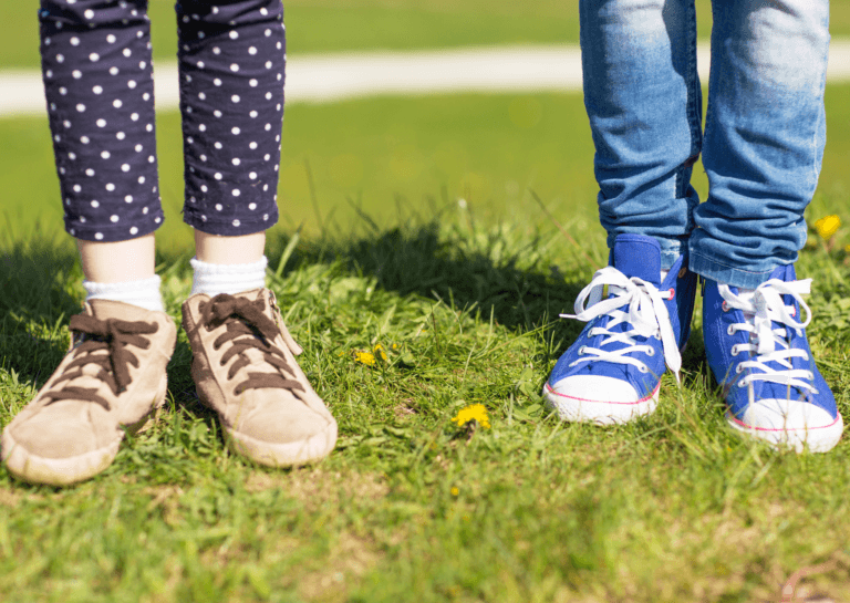 Children's lower legs in long pants and shoes standing on grass, facing towards the camera.