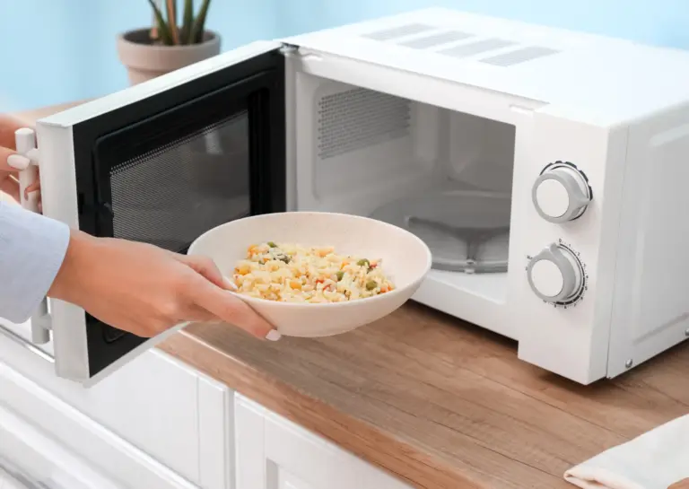 Open microwave countertop oven with someone placing a dish of food inside, demonstrating its functionality.