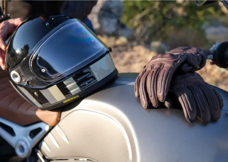 Close-up of a motorcycle seat with a helmet on the saddle and two brown gloves resting on the fuel tank.