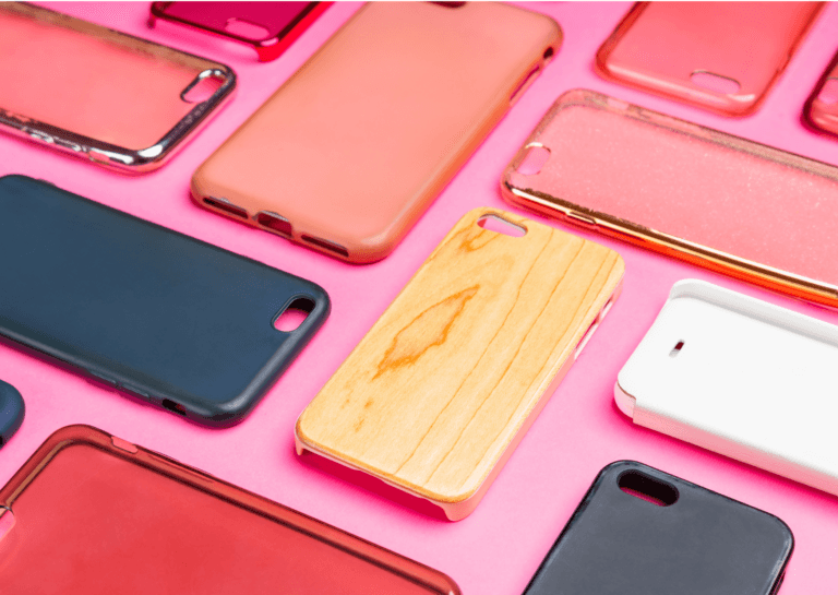 Phone case covers in black, wood-tone, red, white, transparent, and orange, arranged in a 90-degree angle layout on a pink surface.