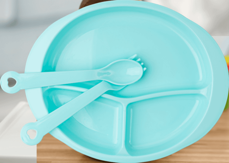 Blue divided toddler plate with a matching plastic fork and knife, arranged neatly on a light background.