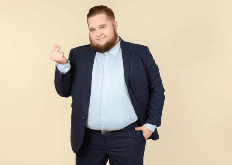 A well-dressed plus-size man wearing a blazer, black belt, and light-colored shirt, with one hand casually in his pocket. His beard adds to his sophisticated look, all set against a cream background that enhances the elegance of his outfit.