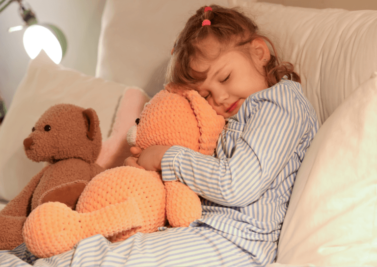 Toddler girl in vertically striped blue and white pajamas, cuddling a stuffed animal with her eyes closed on the couch.