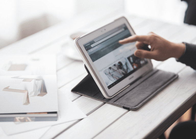 Portable monitor or tablet being operated by a hand pointing at the tablet stand on a table made of horizontal wooden slats.