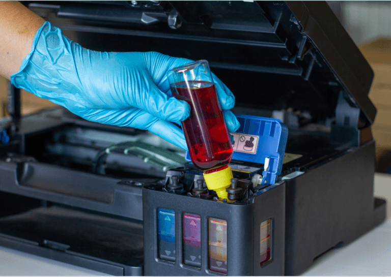 Printer accessories featuring a hand in a blue glove holding a bottle of brown liquid while refilling a printer.