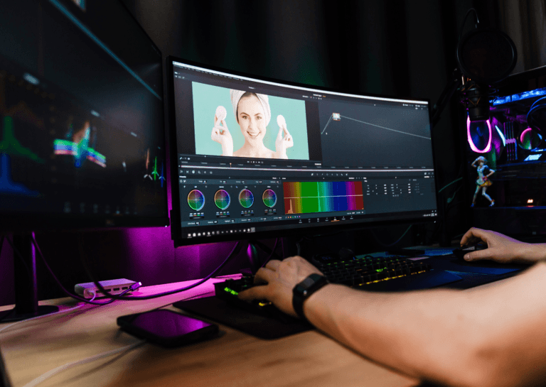 Professional monitors in use, showing a person working with a keyboard and mouse, with editing software displayed on the screens in a dimly lit space.