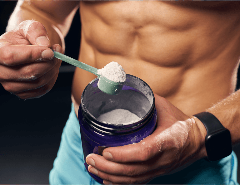 Close-up of a muscular man with visible abs using a scoop to take protein powder from a container, wearing a fitness watch on his wrist.