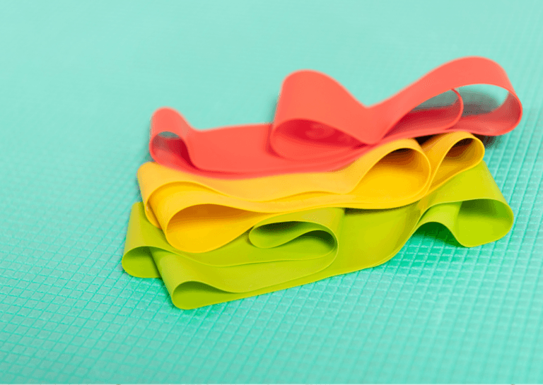 Red, yellow, and green resistance bands stacked on top of each other on a mint-green fitness mat that covers the entire frame, with red on top, followed by yellow and green.