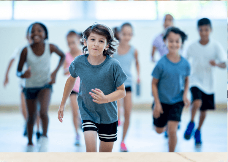 Group of boys and girls around 10 years old, running toward the camera in shorts and short sleeves. Only the center child in front is in sharp focus, with others blurred, resembling a gym class scene.