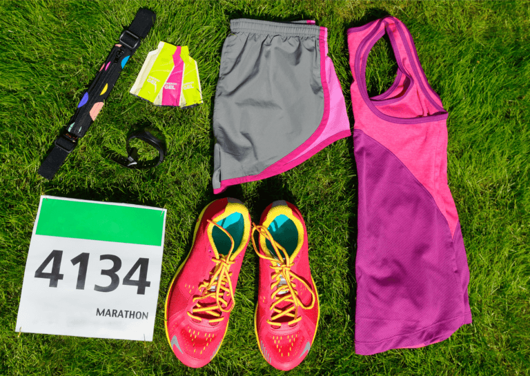 Running gear for a marathon, including race bib number 4134, running shoes, a tank top, shorts, a sports watch, and an energy gel, arranged for a pre-race setup.