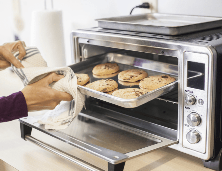 Toaster oven with a baking tray being removed, holding six freshly baked cookies.