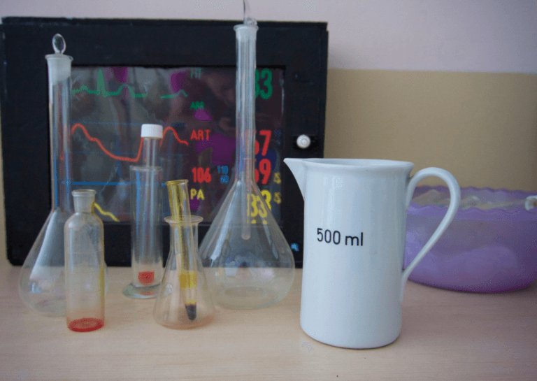 A collection of Erlenmeyer flasks and chemistry elements arranged alongside a porcelain sit pitcher marked '500ml' on a cluttered desk. The scene captures a lively and engaging chemistry workspace, showcasing various tools and equipment.