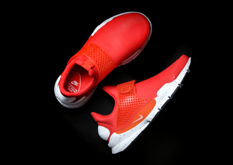 Two red Nike sports shoes photographed from above, with one shoe standing upright and the other lying down, featuring white soles on a dark background.