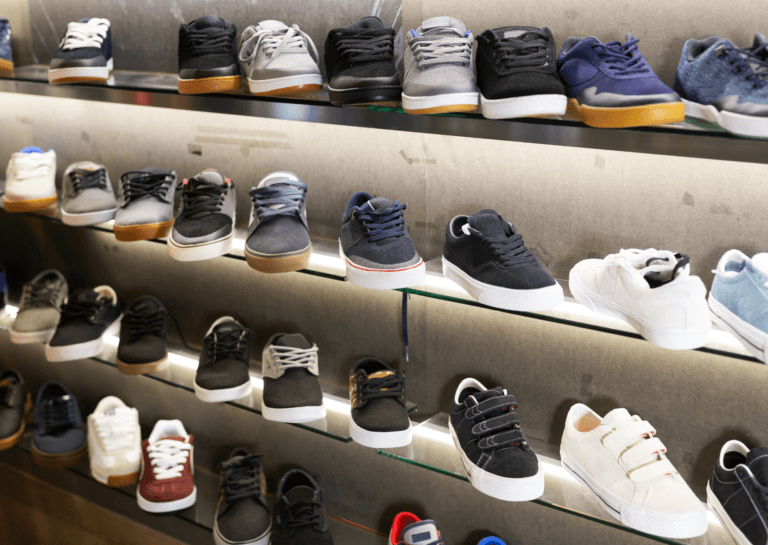 A diverse collection of men's sneakers lined up side by side on various glass shelves, each illuminated by LED strips behind the glass steps. The sleek arrangement highlights the different styles and colors, creating an appealing and modern shopping experience.