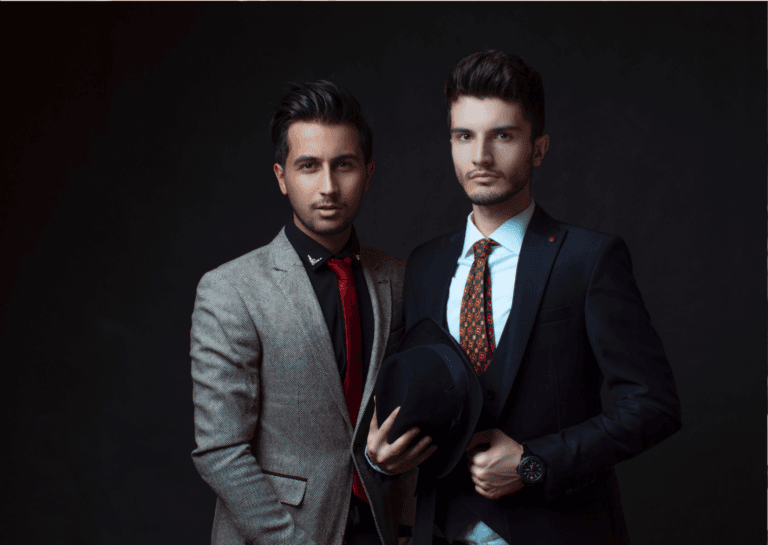 A pair of young men wearing ties and fitted blazers, captured from the waist up against a black background. Their polished appearance and confident posture highlight their sophisticated style, making a strong impression in this elegant setting.